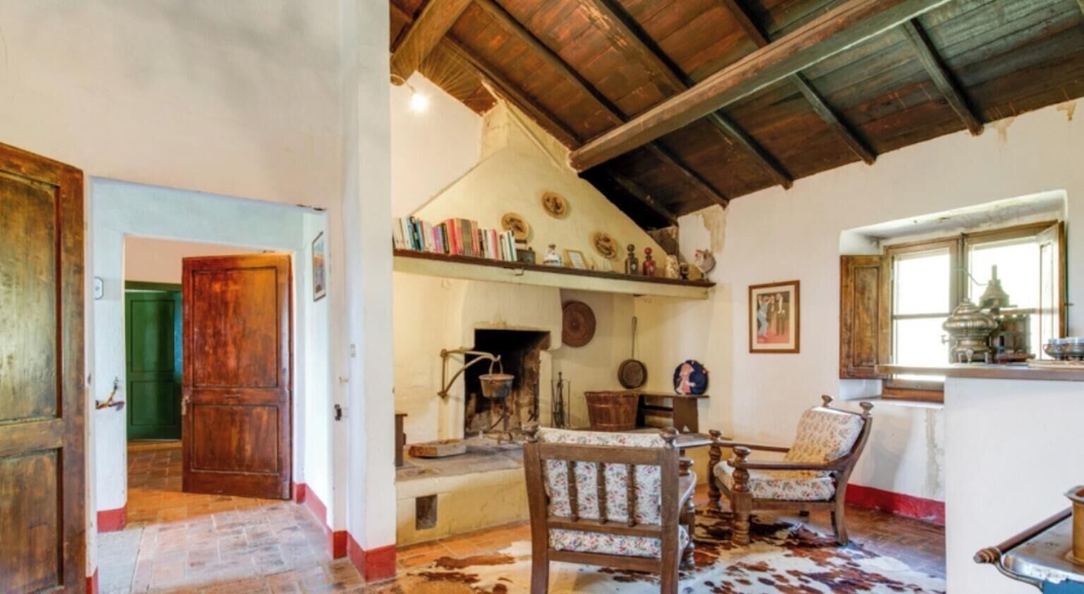 A rustic room with a wooden ceiling, a fireplace, a cowhide rug, and a chair with floral upholstery.