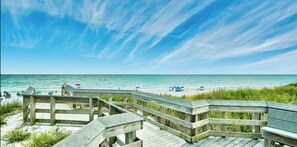 A wooden boardwalk leading to a beach with umbrellas and lounge chairs.