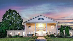 A large, two-story brick building with a central entrance, columns, and a covered porch. - Private 12-Acre Mountain Estate with Blue Ridge Views, Game Room & Sleeps 20 (Fletcher)