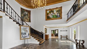 A grand foyer with a marble floor, a staircase with black railings, and two large paintings on the walls. - Private 12-Acre Mountain Estate with Blue Ridge Views, Game Room & Sleeps 20 (Fletcher)