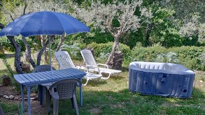 A patio with a table, chairs, a blue umbrella, and a hot tub. - Charmante Maisonnette au Calme (Montmeyan)