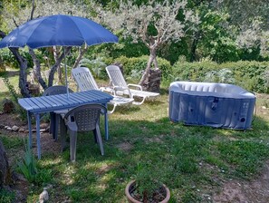 Eine Terrasse mit Tisch, Stühlen, einem blauen Sonnenschirm und einem Whirlpool.