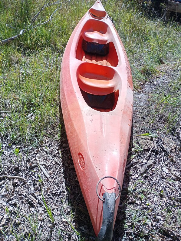 A red kayak with a front paddle resting on the ground.
