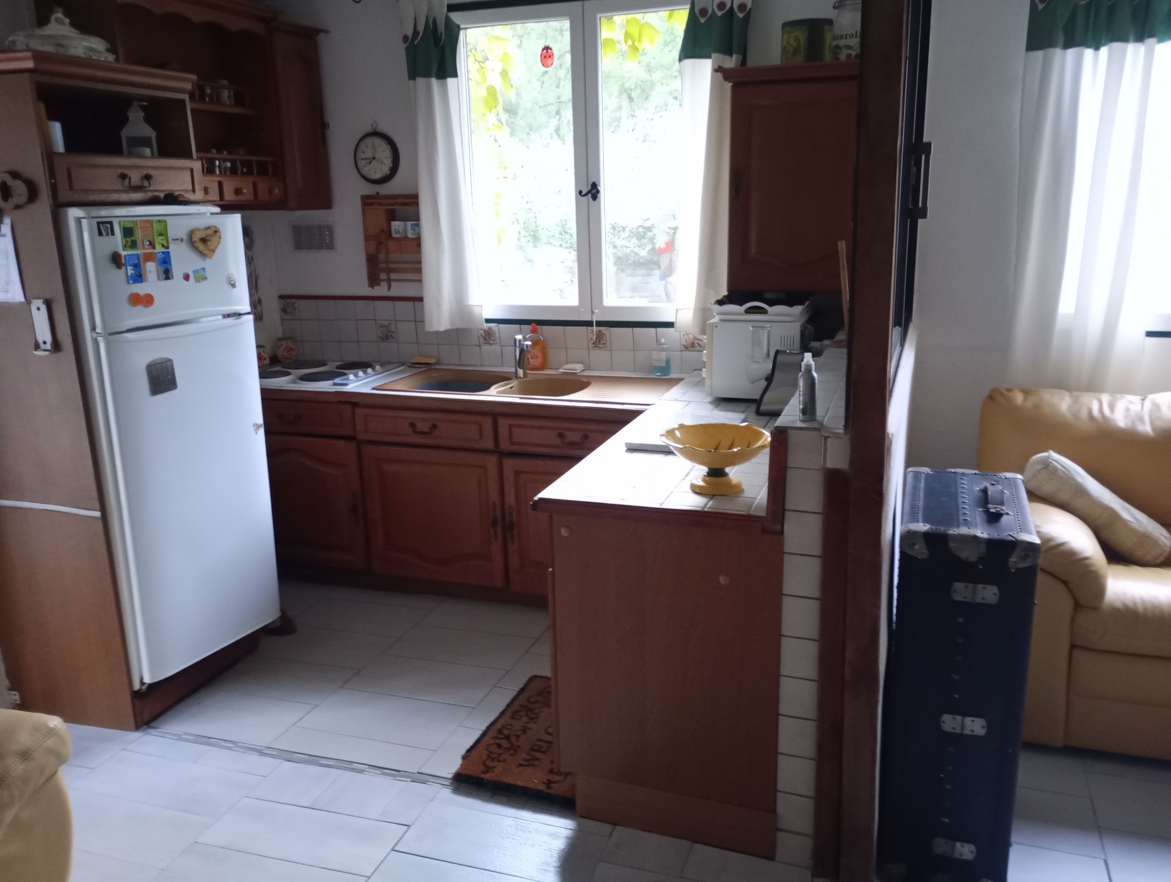 Eine Küche mit Holzschränken, einem weißen Kühlschrank, einer Spüle und einem Fenster mit Vorhängen.