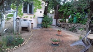 A fenced backyard with a garden, a hose, and a stone wall. - Charmante Maisonnette au Calme (Montmeyan)