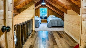 A small attic bedroom with two beds, wooden walls, and a sloped ceiling.