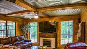 A cozy cabin interior with a leather sofa, a red armchair, a television, and a fireplace.