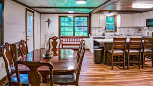 A dining area with a wooden table and chairs, a bench, and a view of the kitchen.