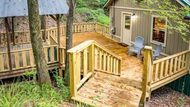 A cabin with a wooden deck, a covered outdoor seating area, and a small porch.