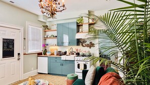 A cozy living room with a sofa, a coffee table, a chandelier, and a kitchen area with cabinets and a stove.