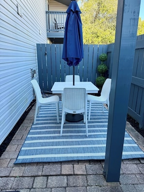 A patio with a table and chairs, a blue umbrella, and a wooden fence. - Walk to Beach - Updated Amelia Island Townhome Near Fort Clinch and Downtown (Fernandina Beach)
