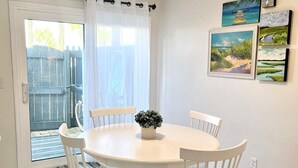 Un coin repas avec une table ronde et des chaises blanches, une plante en pot, et une vue sur le jardin à travers une porte vitrée.