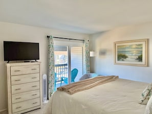A bedroom with a bed, a dresser, a television, a painting, and a view of the outside. - Walk to Beach - Updated Amelia Island Townhome Near Fort Clinch and Downtown (Fernandina Beach)