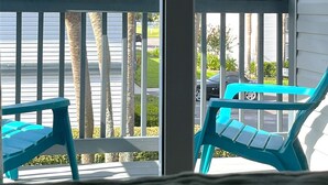 Une véranda avec deux chaises turquoise, des palmiers et une vue sur la rue.