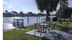 Un patio junto al lago con una mesa, sillas, un banco y una lámpara.