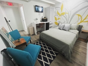 Quarto de hotel com cama, escrivaninha, cadeira, televisão e parede com desenho de folha.