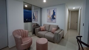 Una sala de estar moderna con un sofá, un sillón y un reposapiés, una puerta de vidrio que da a un balcón, y arte abstracto en la pared.