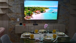Comedor con pared de piedra, televisor de pantalla plana y mesa de vidrio preparada para dos.