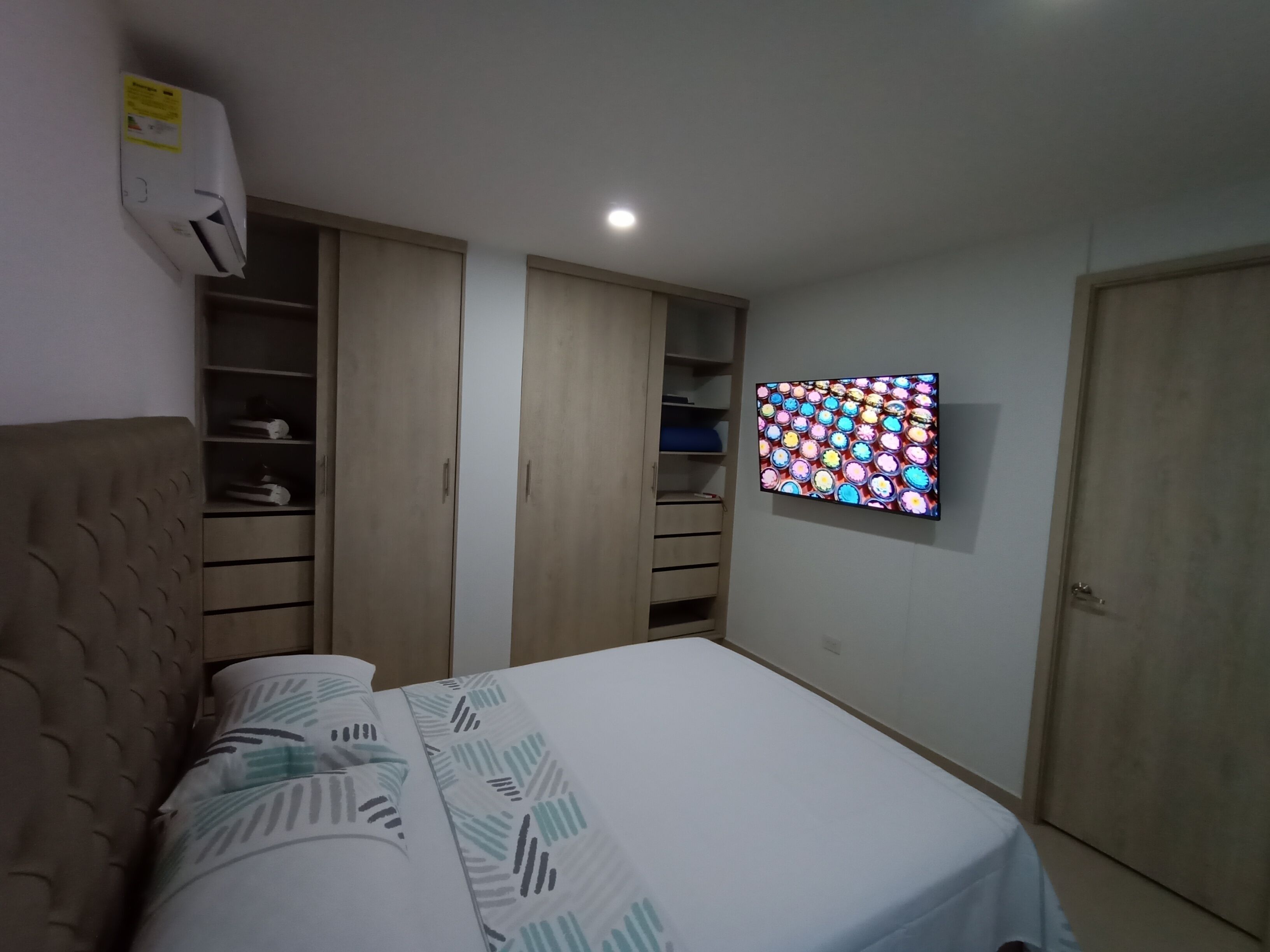 Une chambre à coucher comprenant un lit, une armoire, un téléviseur et un appareil de climatisation.