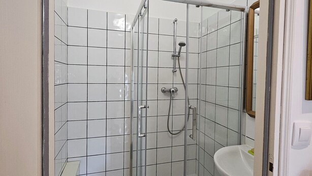 A modern bathroom with a glass-enclosed shower, a white sink, and a tiled floor.