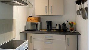 A compact kitchen with a microwave, coffee maker, and kettle on the countertop. There are cabinets below and a stove on the left. - Chambre Giverny (Hargeville)
