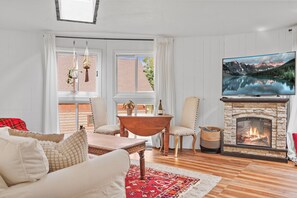 A cozy living room with a fireplace, a television, and a dining area with a table and chairs. - Cozy snow globe like cabin in Blue River forest 7 min to Breck. On bus route! (Breckenridge)