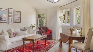 Un salon avec un canapé blanc, un fauteuil rouge, une table basse en bois et un tapis rouge à motifs.