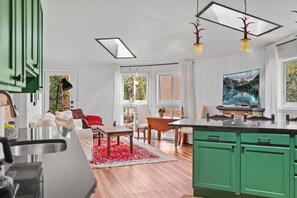 A modern kitchen with green cabinets, a large island, and a dining area with a red rug. - Cozy snow globe like cabin in Blue River forest 7 min to Breck. On bus route! (Breckenridge)