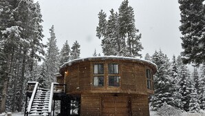 Une cabane en bois à la forme circulaire, entourée d’arbres couverts de neige.