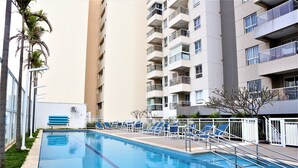 En swimmingpool med solstolar och en hög byggnad i bakgrunden.