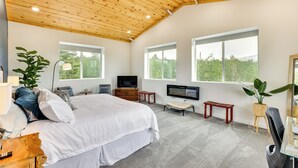 A spacious bedroom with a large bed, a TV, a wooden ceiling, and large windows offering a view of greenery. - Colorado Retreat w/ Gas Grill & Mountain Views! (Fairplay)