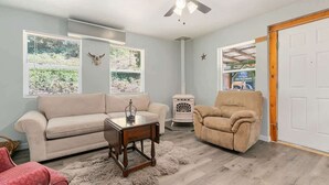 Una sala de estar con un sofá color beige, un sillón rojo, una mesa de centro de madera y un ventilador de techo.