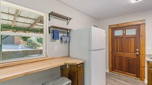 Una cocina compacta con refrigerador empotrado, encimera de madera y ventana con persianas.