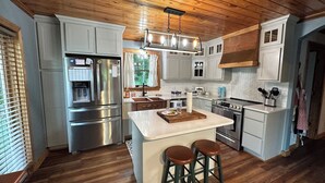 A modern kitchen with wooden ceiling, stainless steel appliances, and a central island with stools.