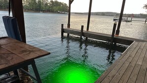 A wooden dock extending into a body of water with a greenish hue, a wooden bench, and a table with a power outlet.