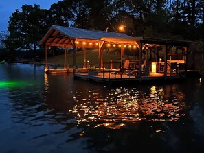 A wooden deck with a covered seating area and a small building with string lights.