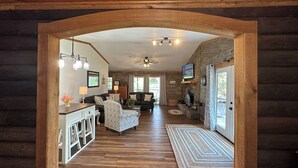 A log cabin interior with a wooden floor, a fireplace, a television, and a ceiling fan.