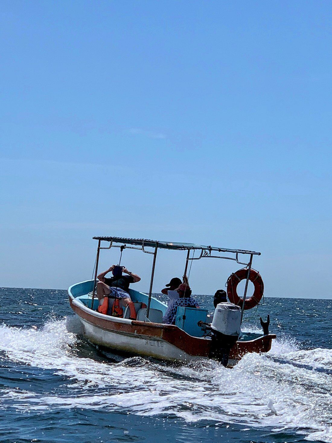 Ein kleines Boot mit Passagieren, einem Rettungsring und einem strahlend blauen Himmel.