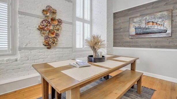 Un comedor con una mesa de madera, paredes de ladrillo blanco y un cuadro en la pared.