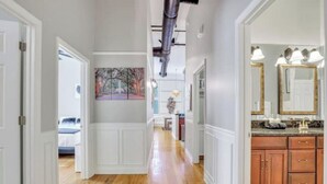 Un pasillo con suelo de madera, paredes blancas y una zona de cocina con armarios de madera y encimera de mármol.