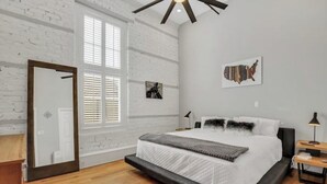 Un dormitorio con una cama grande, suelo de madera, un espejo y una ventana con persianas.