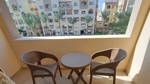 A balcony with wicker chairs and a small round table, overlooking a residential area with multiple buildings and palm trees.