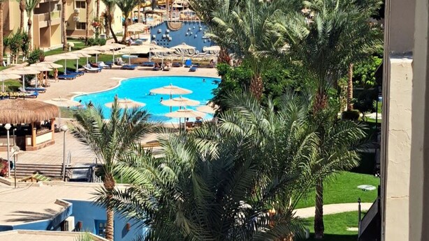 A resort with a large pool, palm trees, and a view of the sea.