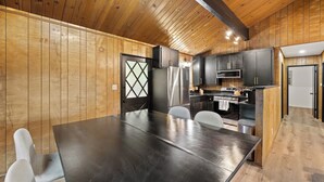 A modern kitchen with wooden paneling, a large dining table, and a built-in oven. - Crestline Lake Gregory Cabin  (Crestline)