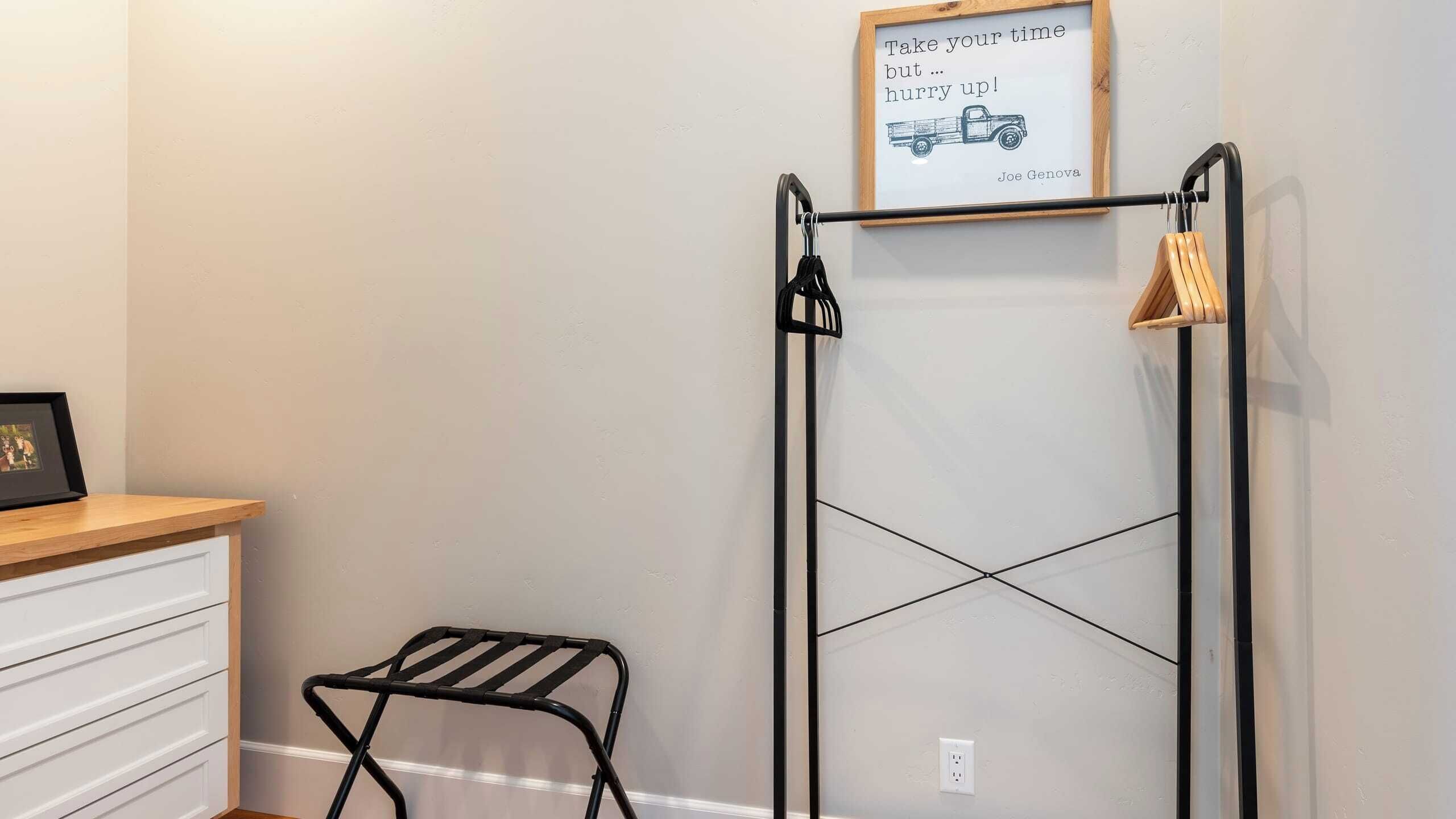 A room with a black metal drying rack, a small stool, a framed quote on the wall, and a wooden shelf.