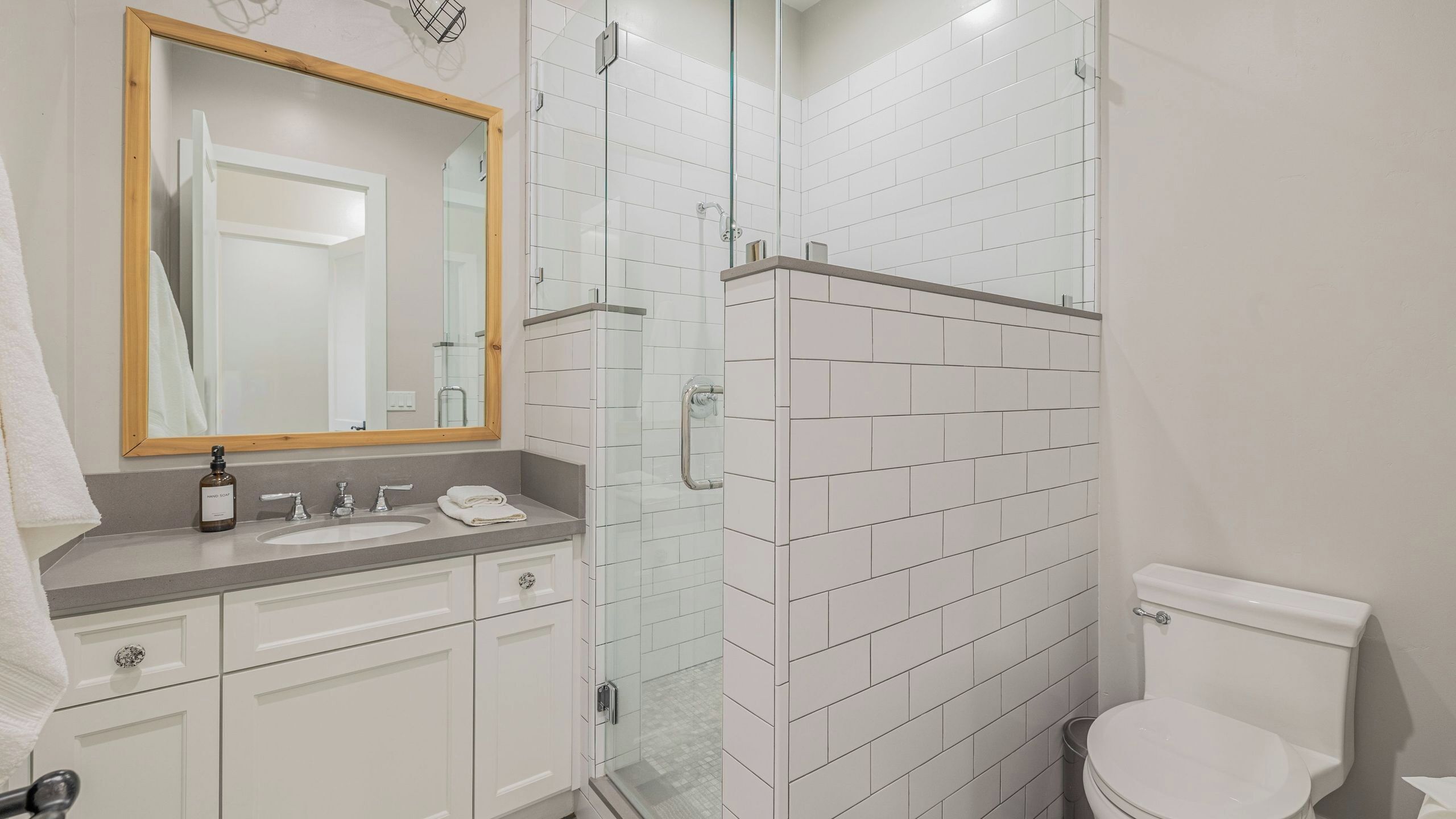 A bathroom with a white sink, mirror, and toilet, and a glass-enclosed shower area.