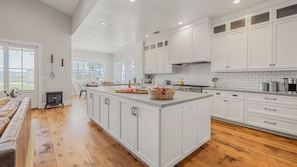 A spacious kitchen with white cabinetry, a large island, and a view of the outdoors.