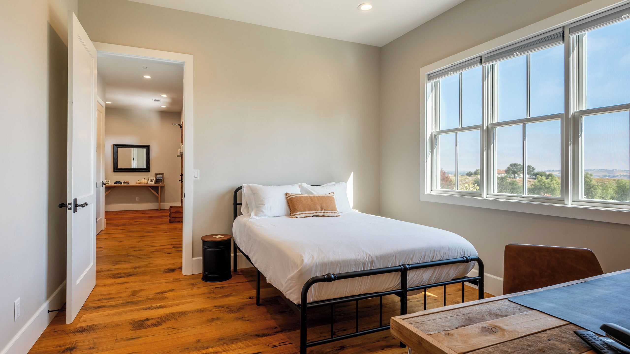 Une chambre à coucher avec un lit, une fenêtre, une table et une porte donnant sur une autre pièce.