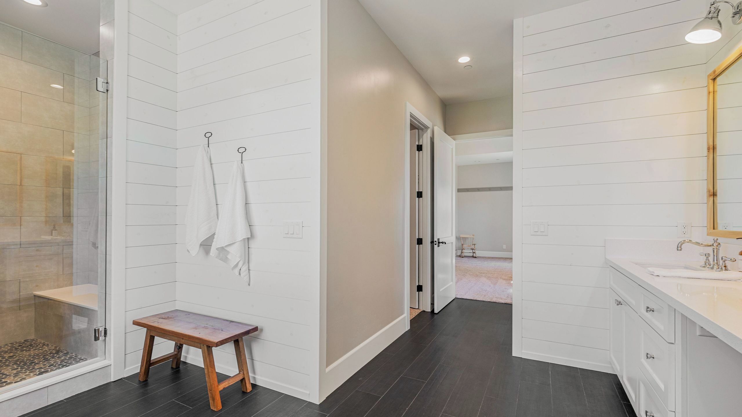 A modern bathroom with a shower, a vanity with a mirror, and a wooden bench.