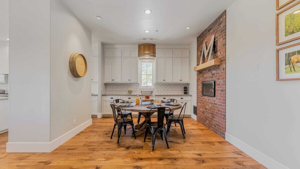 A modern kitchen with white cabinetry, a wooden dining table, and a brick accent wall. - Cooperage by Avantstay Vineyard, Views, Soccer (Paso Robles)